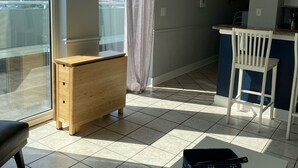 A modern apartment with a balcony, a wooden dresser, a white table, and a kitchen area. - Oceanfront W/Long Range Views, 2 bed, 2 bath Penthouse, Large Balcony, Sleeps 6 (Myrtle Beach)