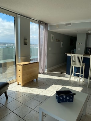 A modern apartment with a balcony, a wooden dresser, a white table, and a kitchen area.
