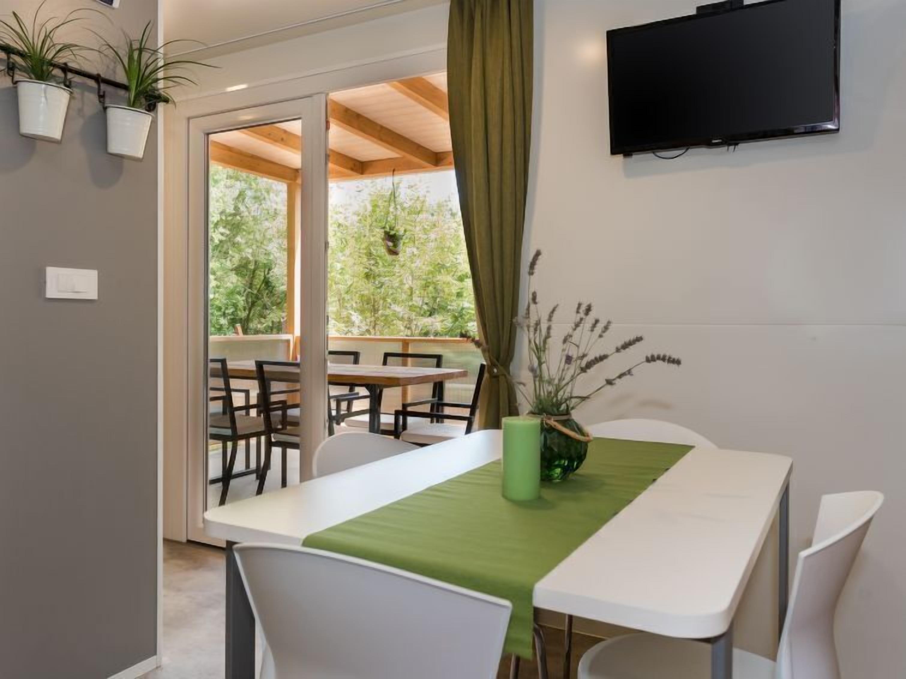 A modern dining area with a table set for two, a green table runner, and a potted plant on the table.
