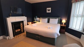 Une chambre à coucher avec un grand lit, une cheminée, une table de chevet et une fenêtre avec des stores.