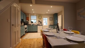 Una cocina moderna con armarios azul verdoso, un microondas y un lavavajillas. Hay un comedor con una mesa preparada para cuatro, incluyendo copas de vino y una botella de champán.