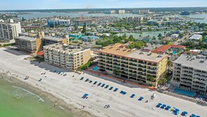 Un paisaje urbano costero con un hotel frente a la playa, que cuenta con varios balcones, una piscina y vistas al mar.