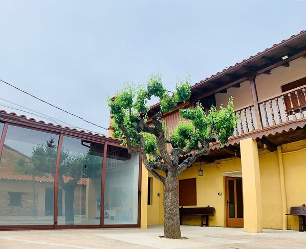 Un edificio con balcón, un árbol en primer plano y una banca.