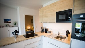 Una cocina moderna con armarios blancos, encimera de madera, microondas integrado, cafetera y lavabo.