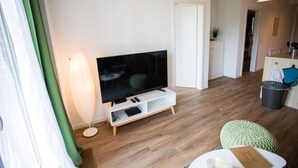 Una sala de estar moderna con un televisor de pantalla plana sobre un mueble blanco, una lámpara de pie y un otoman verde.