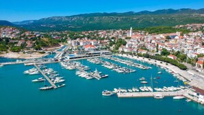 A coastal town with a marina filled with boats, surrounded by residential buildings and mountains in the background.