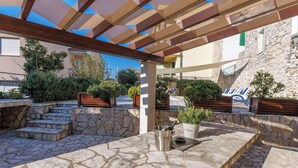 An outdoor patio area with stone flooring, wooden benches, and potted plants.