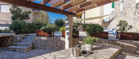 Un patio al aire libre con suelo de piedra, bancos de madera y plantas en macetas.