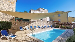 A pool area with stone flooring, blue lounge chairs, and a stone wall.