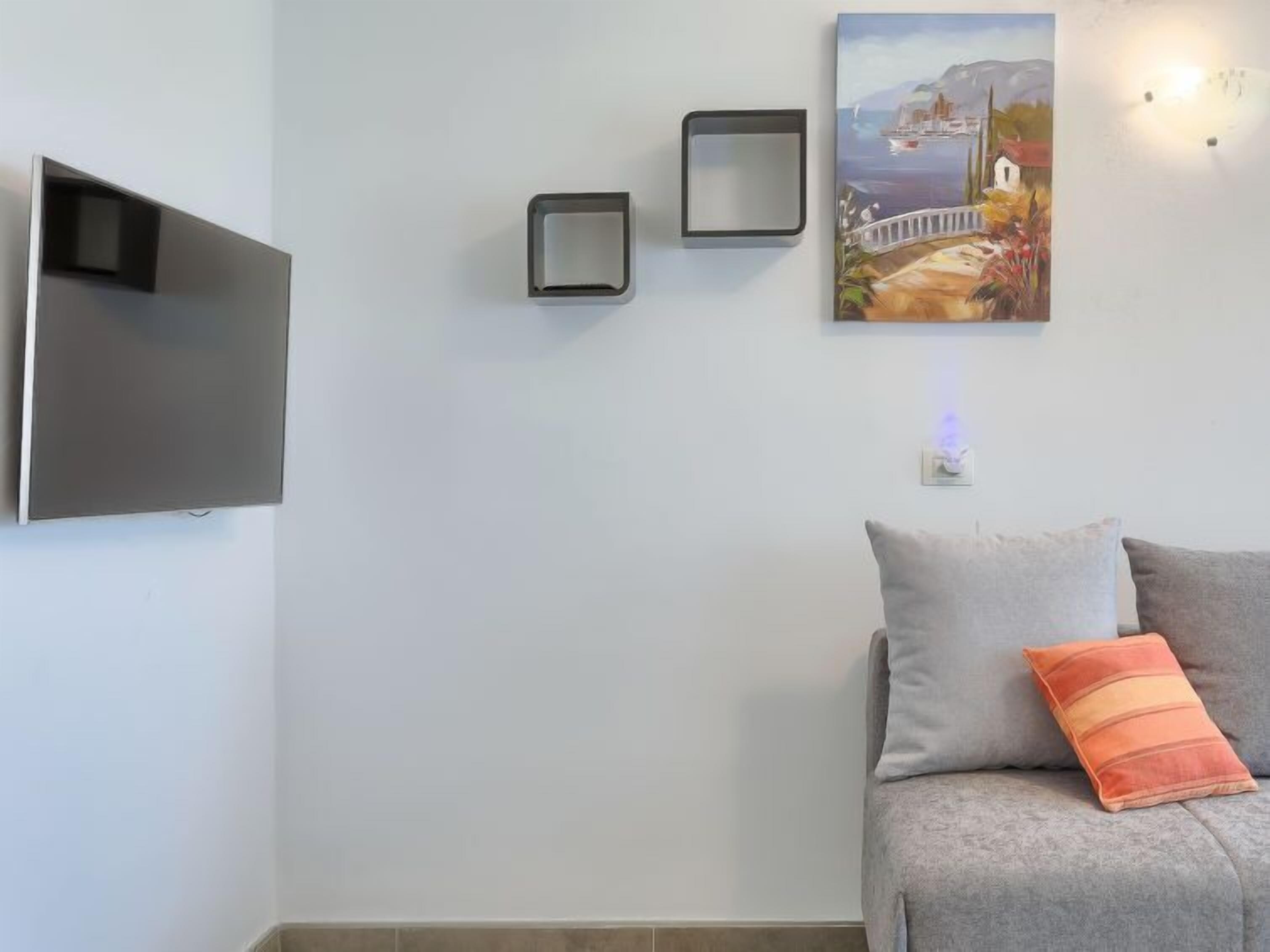 Un salon moderne avec un téléviseur à écran plat fixé au mur, une petite table et un tableau représentant un paysage côtier.