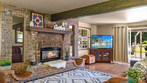 A living room with a brick fireplace, a television, and a cozy seating area. - Heated pool,4 bedrooms,hot tub, Dogs ok, pond, 2mls to town (Leavenworth)