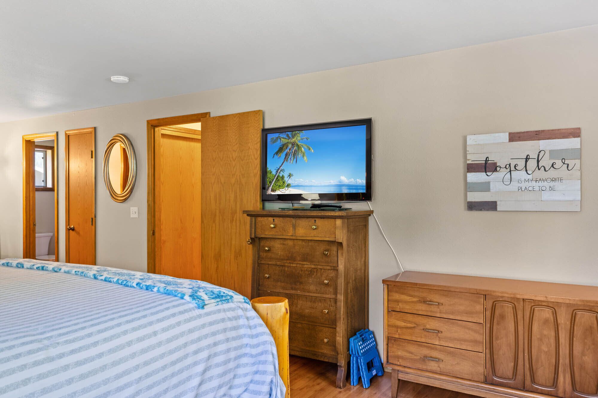 A bedroom with a bed, a wooden dresser, a television on a stand, a mirror, and a wall with a motivational quote.