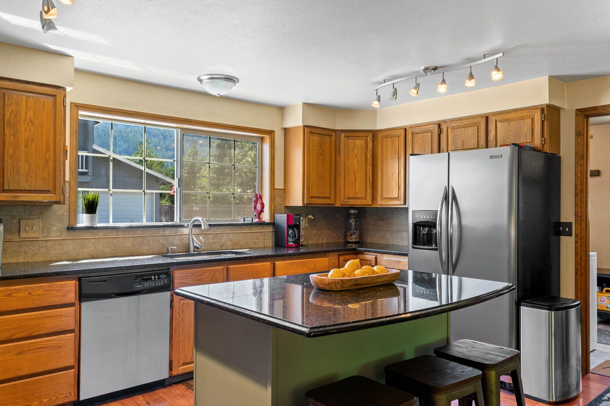 A kitchen with wooden cabinets, a stainless steel refrigerator, a coffee maker, and a window with a view of the outdoors.