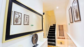 A hallway with a framed artwork, a white console table with a decorative object, and a staircase with a railing. - Magical & Charming 8 rooms Covent Garden TownHouse (London)