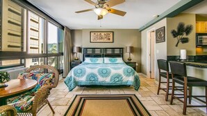 A bedroom with a bed, a ceiling fan, a window, a dining table, and a kitchen area. - @ Marbella Lane - Mountain View Studio (Honolulu)