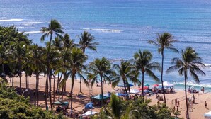 A beach with palm trees, umbrellas, and people. - @ Marbella Lane - Mountain View Studio (Honolulu)