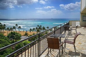 A balcony with wicker furniture overlooking a beach with palm trees and the ocean.