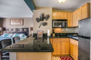 A compact kitchen with a microwave, refrigerator, wooden cabinets, and a central island with a marble countertop.
