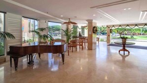 A spacious lobby with a grand piano, wooden chairs, and a round table. - @ Marbella Lane - Mountain View Studio (Honolulu)
