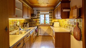 Cuina amb armaris de fusta, respatller de rajoles i finestra amb cortines.