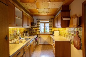 Una cocina con armarios de madera, salpicadero de azulejos y una ventana con cortinas.