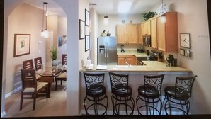 A modern kitchen with wooden cabinets, a central island with bar stools, and pendant lighting.