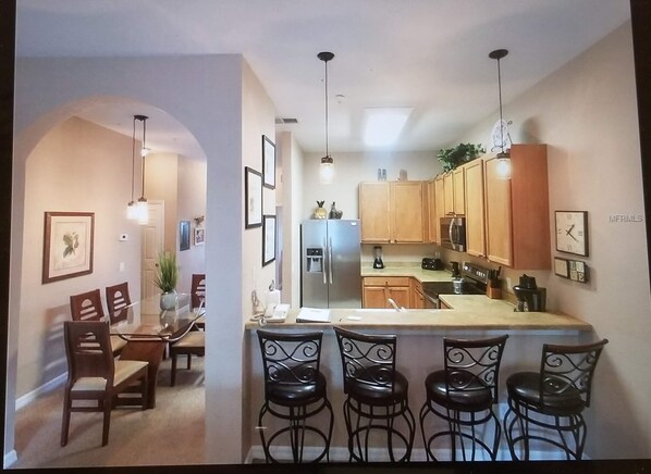 A modern kitchen with wooden cabinets, a central island with bar stools, and pendant lighting.