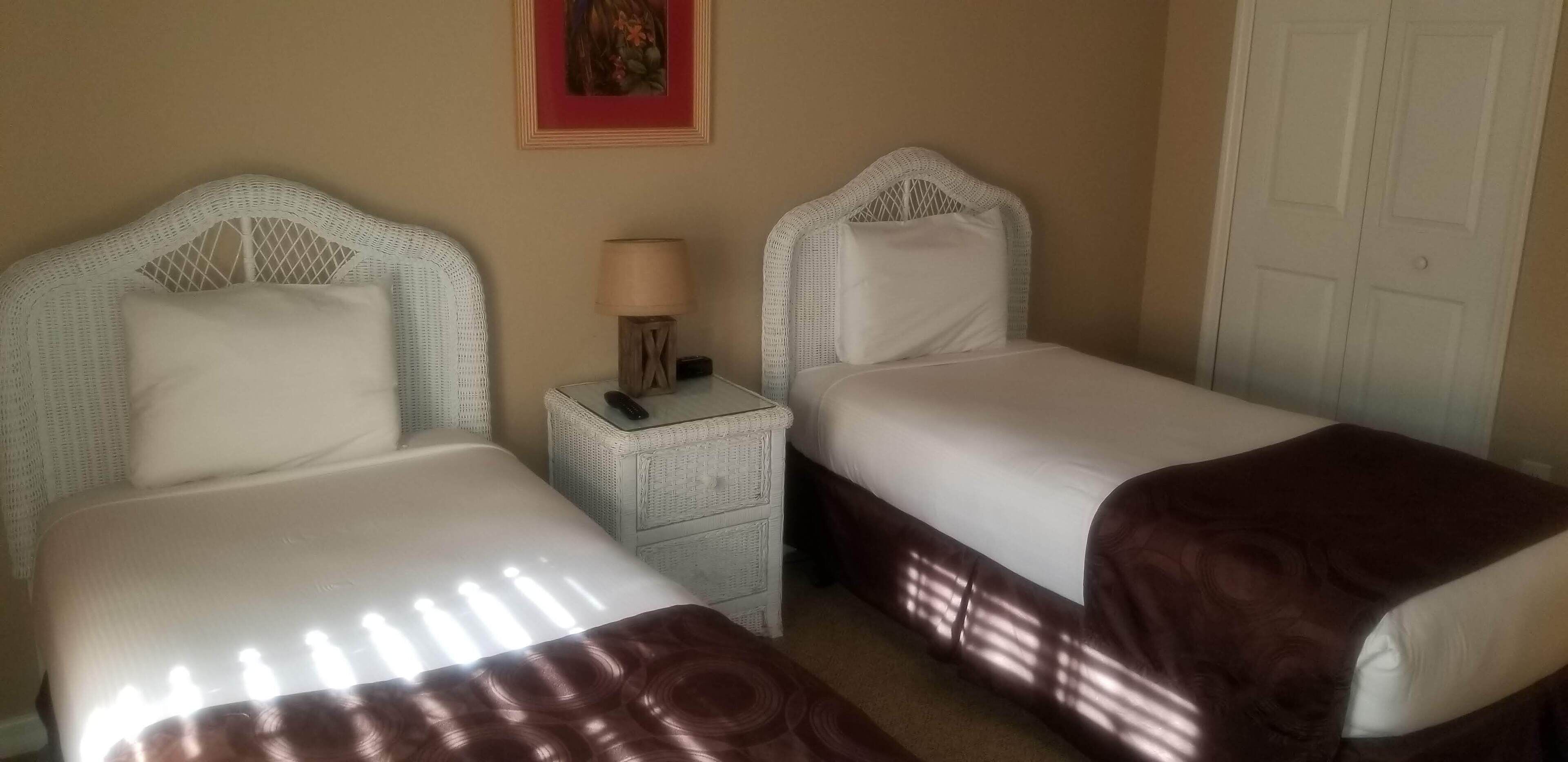 A hotel room with two single beds, a nightstand with a lamp, and a door.