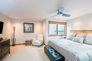 A bedroom with a bed, a chair, a dresser, a ceiling fan, and a window.