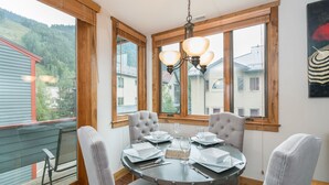Un coin repas avec une table ronde dressée pour quatre personnes, entourée de chaises rembourrées, et un lustre au-dessus.