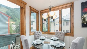 A round dining table with four chairs, a chandelier, and a view of houses through large windows. - Telluride Lodge Condo #538 (Telluride)