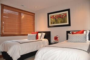 Two single beds with white bedding and patterned pillows, set against a dark headboard, with a framed artwork above.