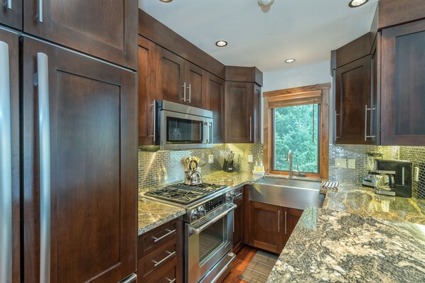 Equipped with a gas stove, microwave, oven, and sink, this kitchen offers a well-lit space with a window overlooking the outdoors.