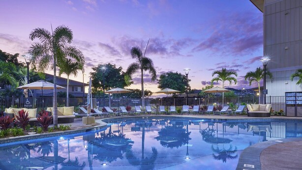 A pool area with lounge chairs and umbrellas, surrounded by palm trees and a building. - Residence Inn by Marriott Oahu Kapolei (Kapolei)