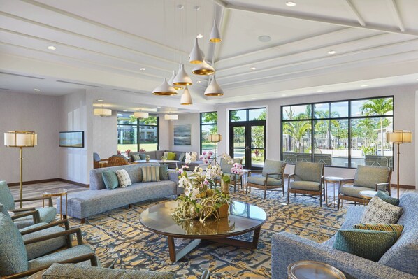 A spacious lobby with a round coffee table, sofas, and chairs arranged around a central area. Large windows provide a view of the outdoors. - Residence Inn by Marriott Oahu Kapolei (Kapolei)