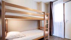 A bunk bed with a wooden frame and white bedding in a room with a door and curtains. - Studio de Montagne Cosy | 250m des Commerces (Pra Loup)