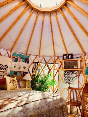 A yurt interior with a bed, a chair, a lamp, and various wall decorations. - The YOGA YURTA... Extremely Civilized Glamping at SUNNY MELLOW ECO VILLA! (Village of Tijeras)