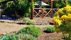 A wooden pergola with a sign reading "Sunny-Mellow Vineyard" surrounded by lush greenery and flowering plants. - The YOGA YURTA... Extremely Civilized Glamping at SUNNY MELLOW ECO VILLA! (Village of Tijeras)