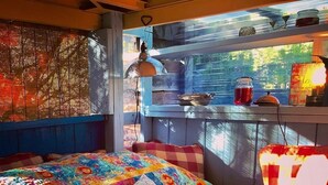 Una habitación acogedora con una colcha de patchwork colorida, una ventana con persianas y un estante con diversos objetos.