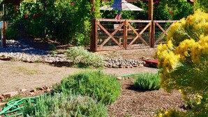 Una pérgola de madera con un letrero que dice "Sunny-Mellow Vineyard", rodeada de exuberante follaje y plantas florecientes.