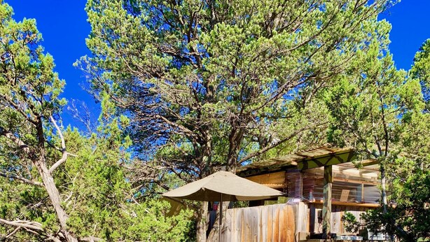 Una cabaña rústica con terraza de madera, rodeada de árboles y un espacio para fogata.