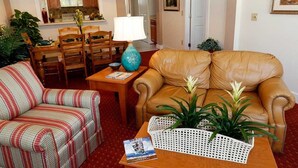 En stue med en stribet lænestol, en brun lædersofa, et lille bord med en lampe og en potteplante.