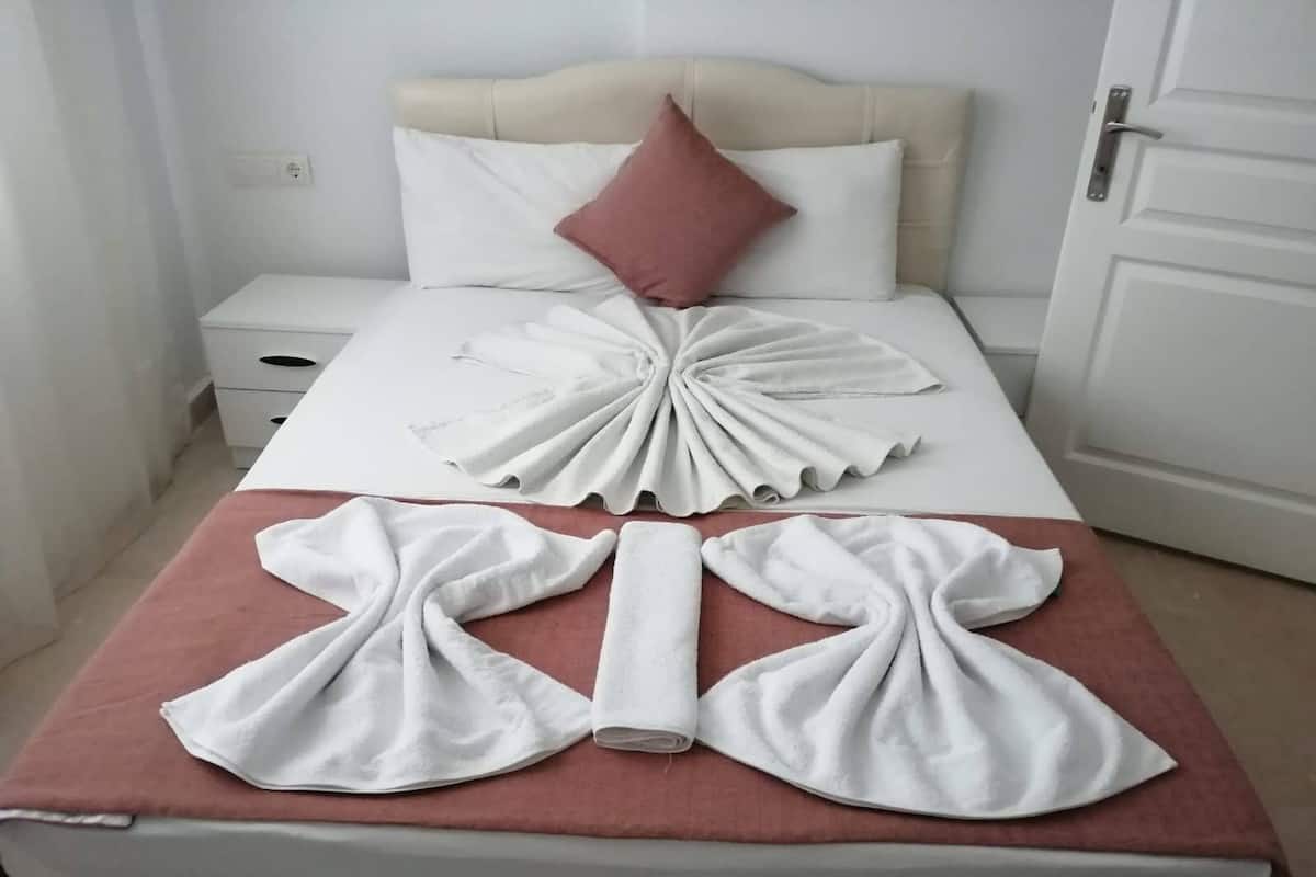 A neatly made bed with a white and pink color scheme, a folded white towel on the bed, and a white towel on the floor.