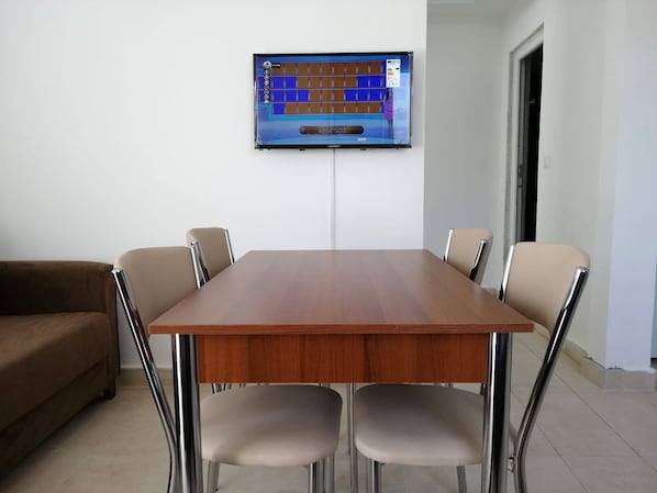 Un salón de conferencias con una mesa de madera, cuatro sillas, un televisor montado en la pared y un sofá marrón.