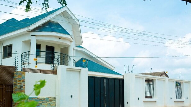 A modern two-story house with a large garage door, a balcony, and a white exterior. - Beautiful Secure Home With 24 hour Security (Accra)
