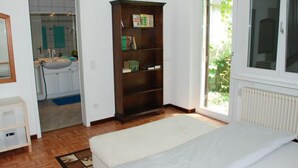 Une chambre à coucher avec un lit, une bibliothèque en bois, une fenêtre donnant sur un paysage verdoyant et une salle de bain visible à travers une porte ouverte.