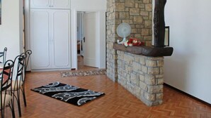 Un couloir avec une cheminée en pierre, des meubles blancs et un coin repas agrémenté d’un tapis à motifs.