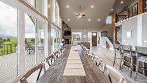 A spacious dining area with a long wooden table, multiple chairs, and a view of a deck and landscape. - Foxridge (Sleeps 34) by Bear Lake Luxury Rentals (Garden City)