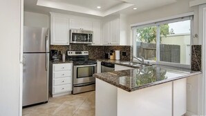 Una cucina moderna con mobili bianchi, elettrodomestici in acciaio inossidabile, piani di lavoro in granito e un'ampia finestra.