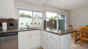 Una cucina moderna con mobili bianchi, piani in granito, lavastoviglie integrata e un'ampia finestra con cesti di fiori appesi.
